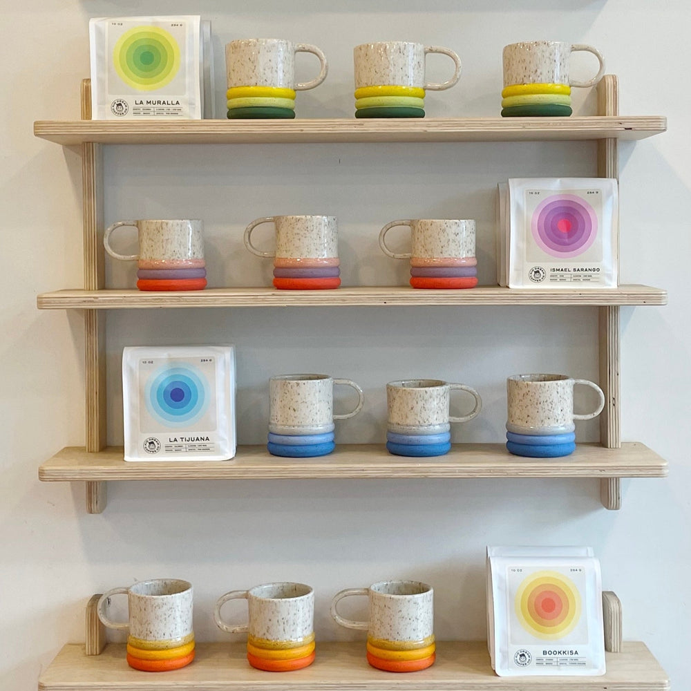 Wooden shelves displaying ceramic mugs with colorful glazes and coffee beans.